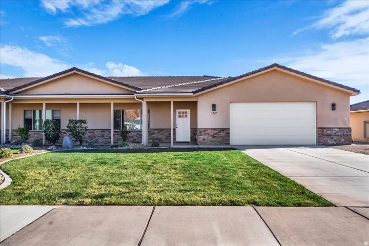 Ranch-style house with stucco siding, stone siding, an attached garage, and a front lawn