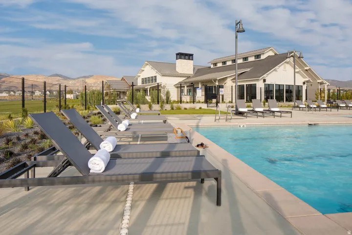Resort-style swimming pool with a surrounding concrete deck, multiple lounge chairs, and a contemporary clubhouse building featuring extensive glazing