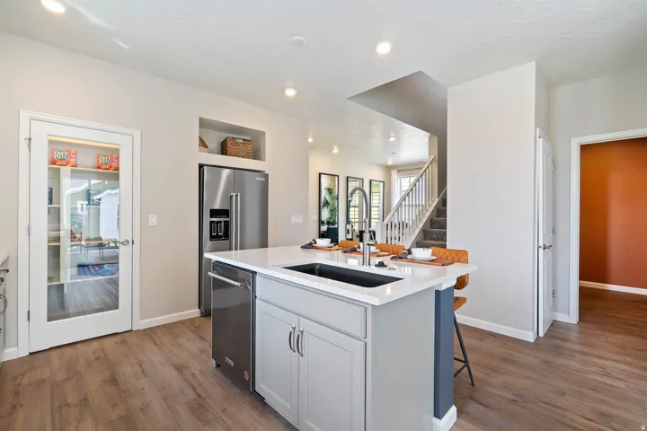 Kitchen featuring wood-finish flooring, stainless steel appliances, a center island with sink, recessed lighting, and a pantry with a glass-paneled door