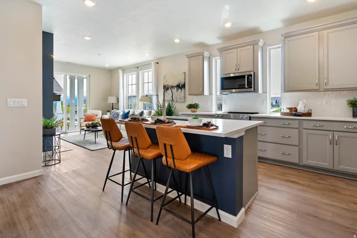 Wood-finish flooring, recessed lighting, kitchen island with a white countertop, light gray cabinetry, and a white herringbone tile backsplash