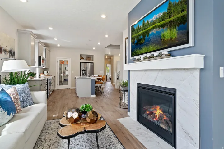 Living area featuring a fireplace with a white mantel, tile surround, and an open-concept kitchen with light cabinetry, stainless steel appliances, and wood-finish flooring
