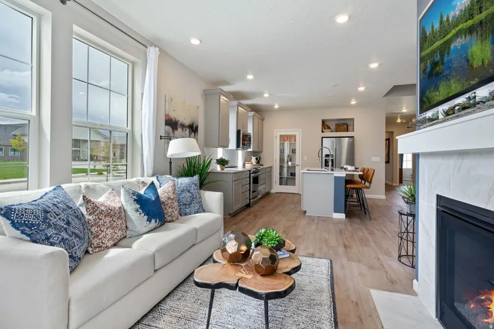Open-concept living space featuring large windows, wood-finish flooring, a fireplace with a tiled surround, a kitchen island with seating, and stainless steel appliances