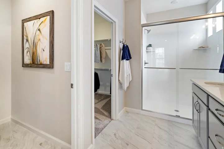 Walk-in shower with glass enclosure, single vanity with light-toned countertop, and tile flooring