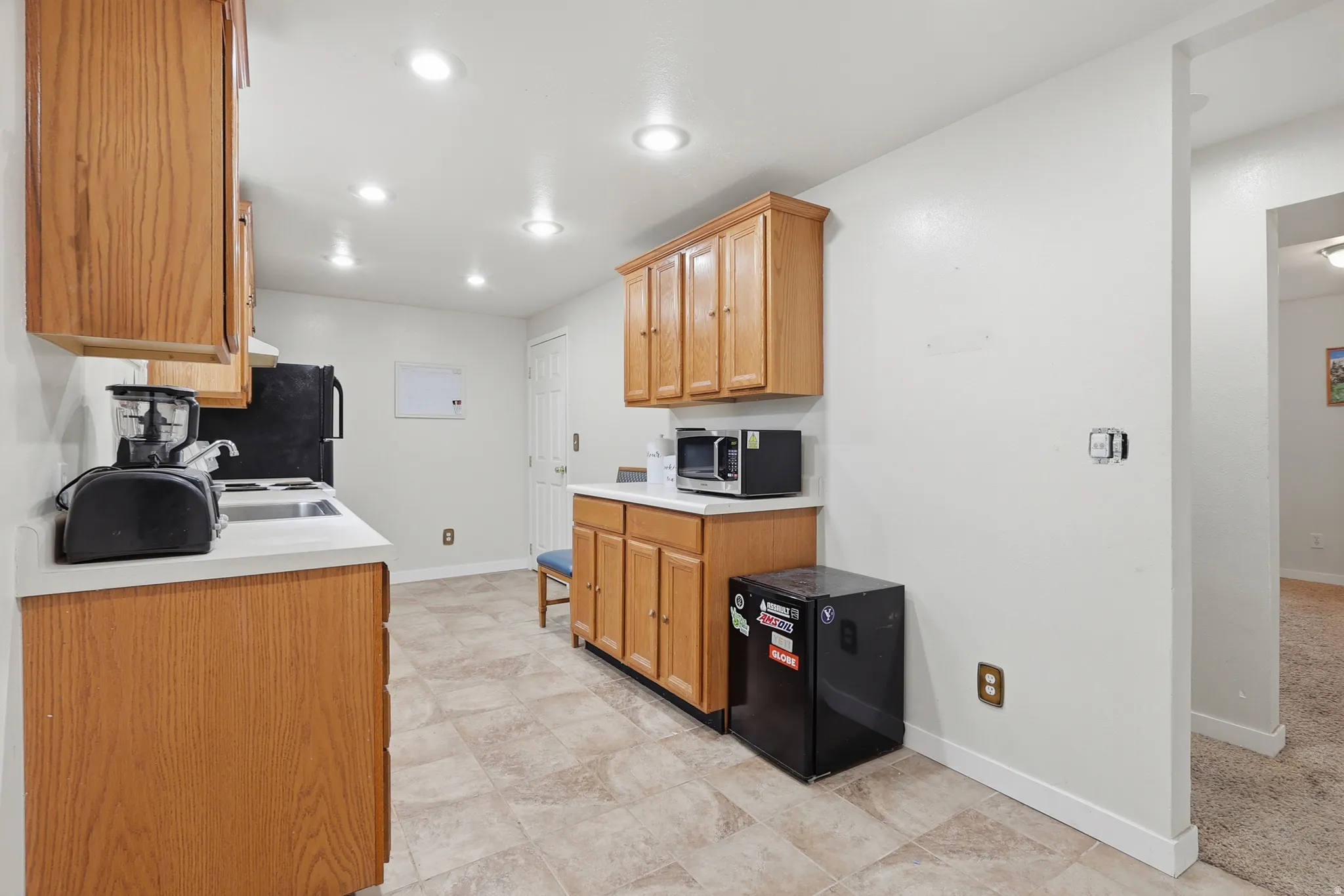 Kitchen featuring light countertops, black refrigerator, freestanding refrigerator, stainless steel microwave, and recessed lighting