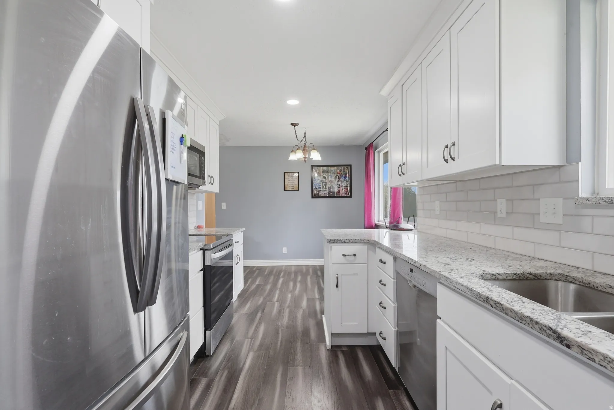 Kitchen with stainless steel appliances, white cabinets, light stone countertops, and a dining room chandelier