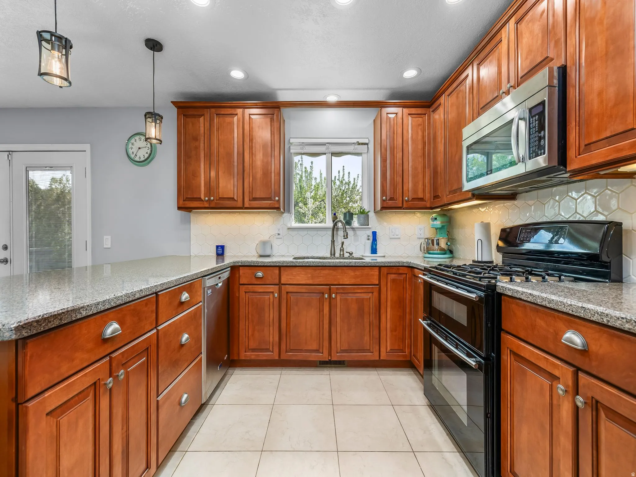 Kitchen featuring stainless steel appliances, wood finish cabinets, light stone counters, a peninsula, and decorative light fixtures