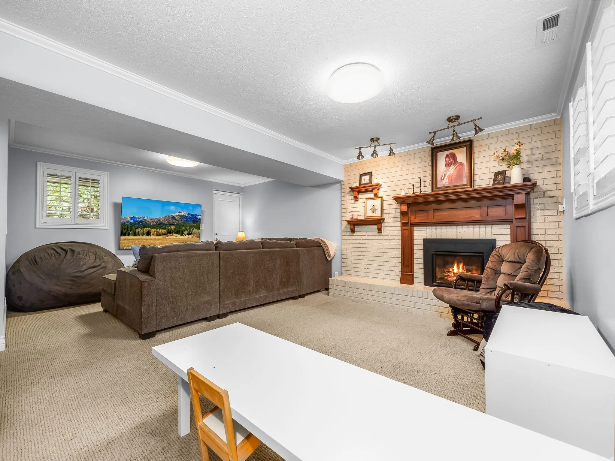 Living area featuring carpet, brick wall, a brick fireplace, crown molding, and a textured ceiling