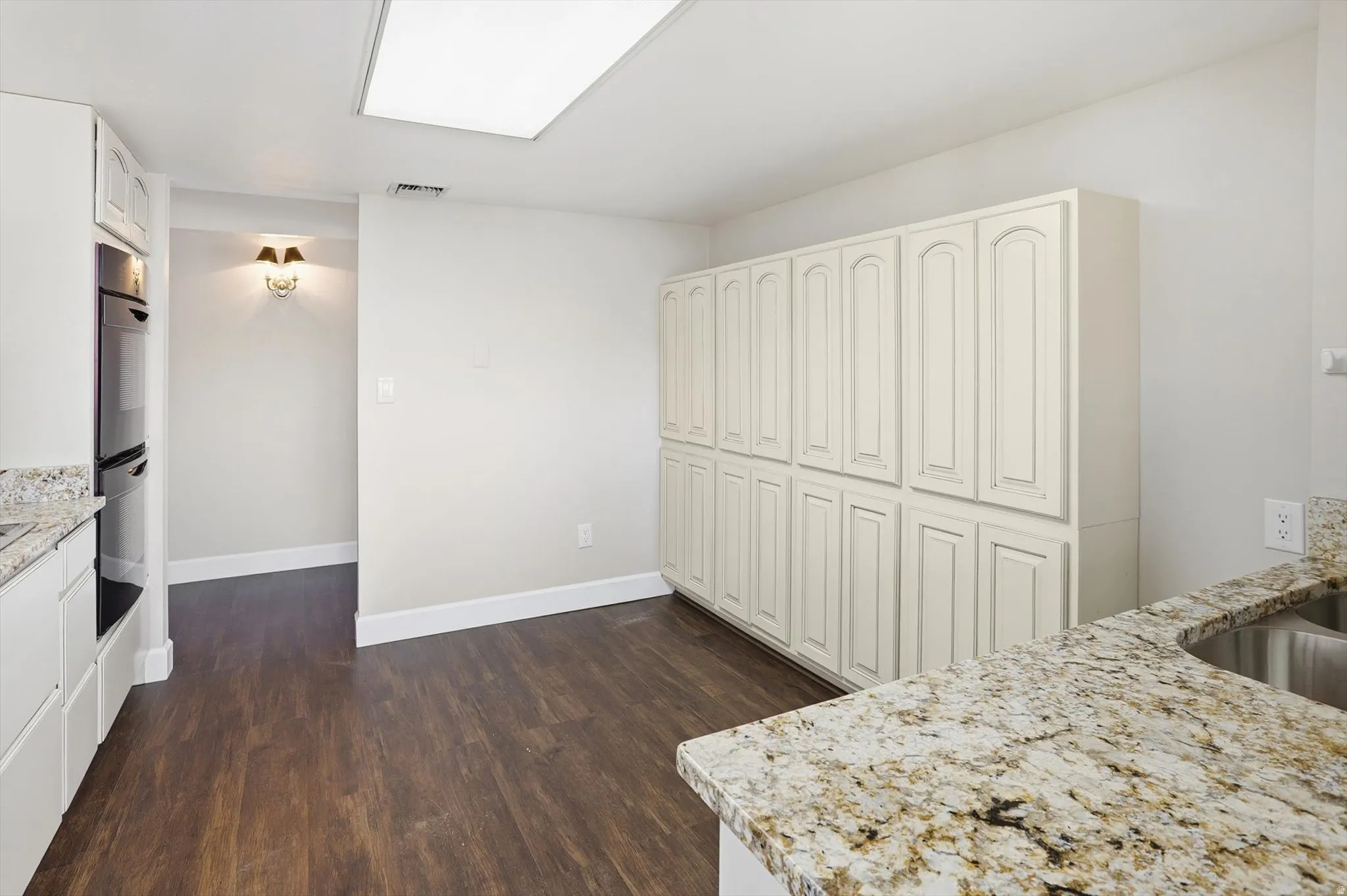 Kitchen featuring light stone counters, dark wood-style flooring, double oven, and white cabinets