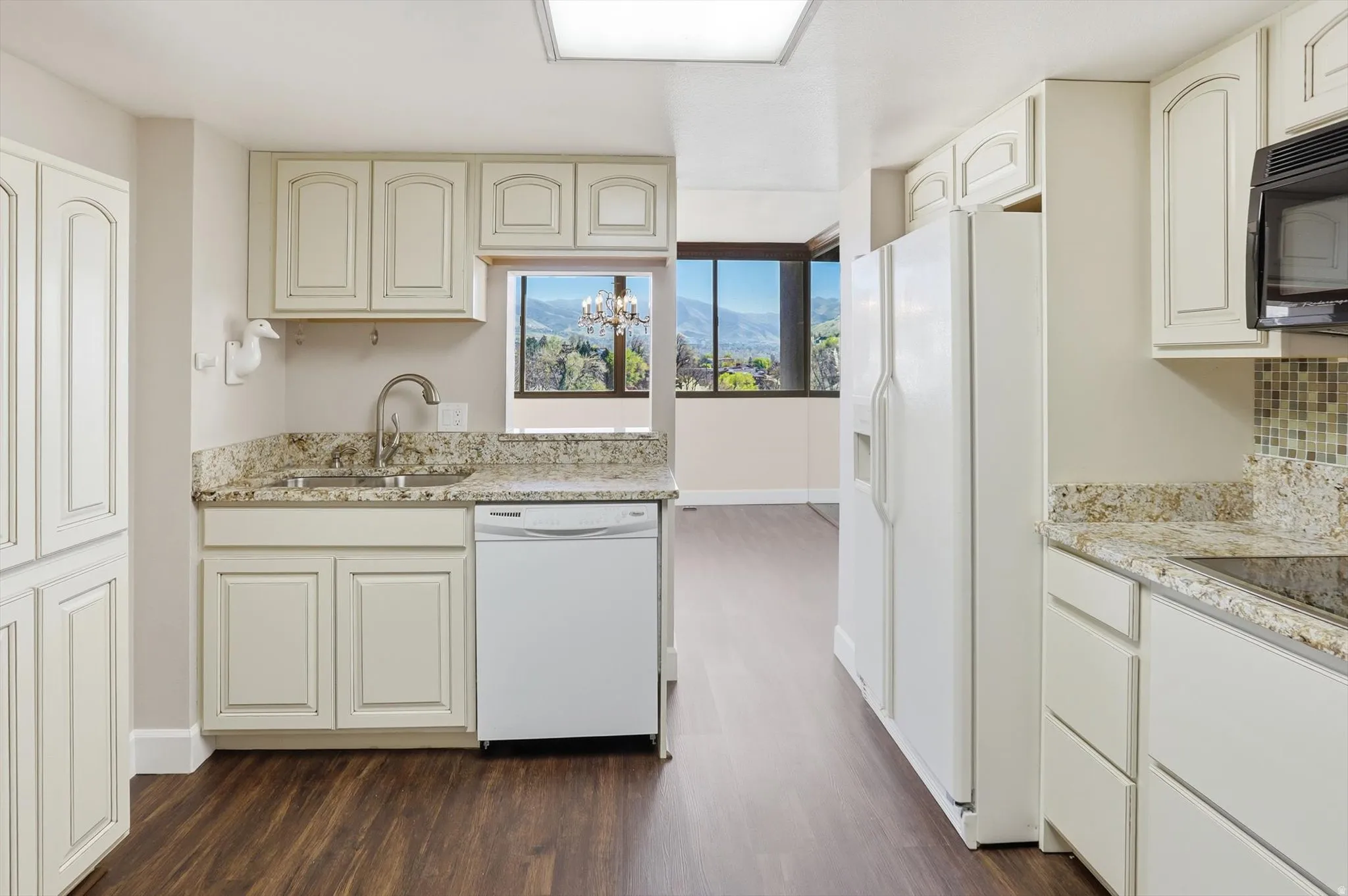 Kitchen with white appliances, light stone countertops, dark wood-type flooring, cream cabinetry, and a mountain view
