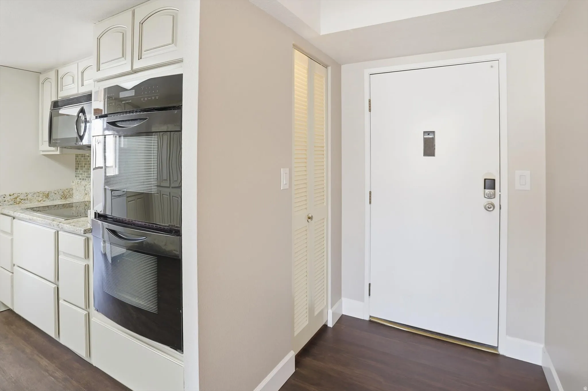 Kitchen featuring black appliances, dark wood-style flooring, white cabinetry, and light stone countertops