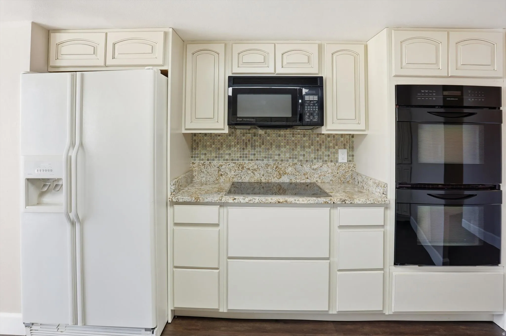 Kitchen with black appliances, cream cabinetry, light stone counters, and dark wood-type flooring