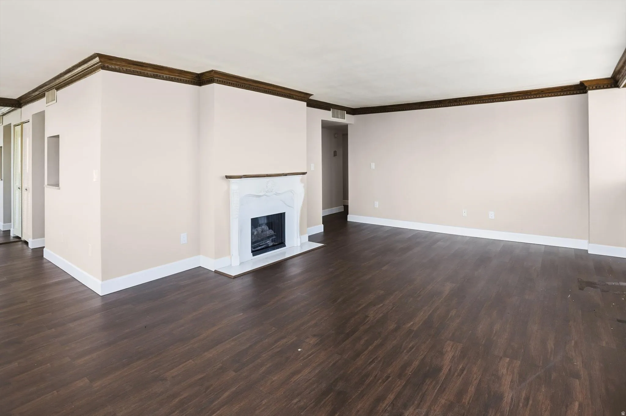 Unfurnished living room featuring a high end fireplace, ornamental molding, and dark wood-type flooring