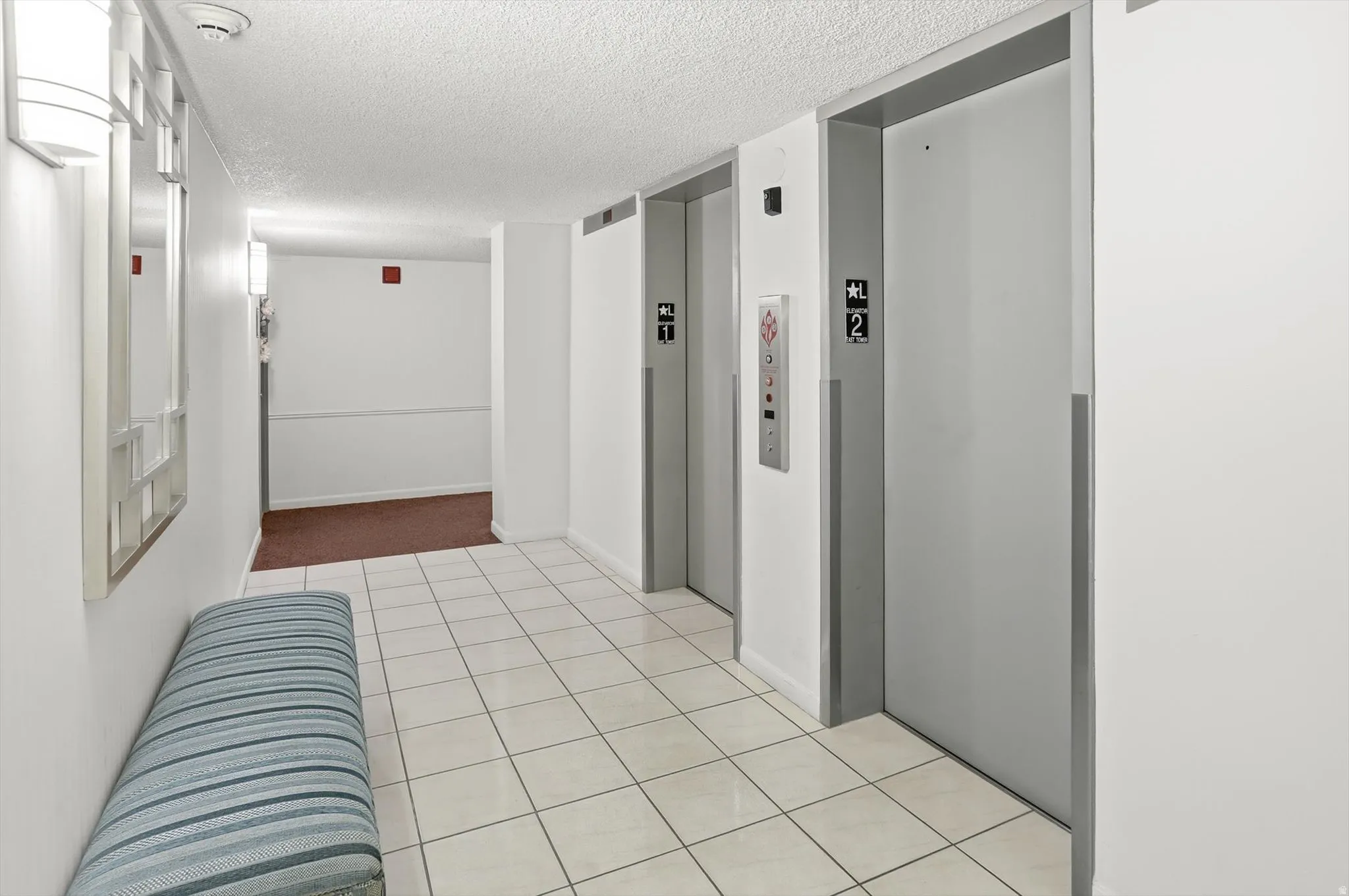 Hallway with a textured ceiling, elevator, and light tile patterned flooring