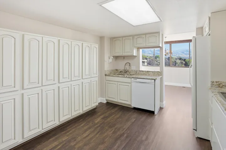 Kitchen with light stone counters, white appliances, and dark wood-type flooring