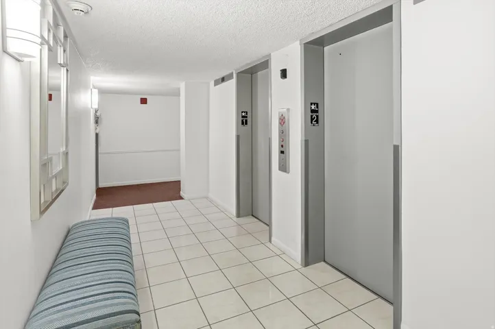 Hallway with a textured ceiling, elevator, and light tile patterned flooring