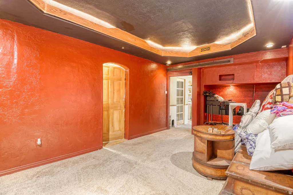 Carpeted living area featuring a tray ceiling, arched walkways, and a textured wall