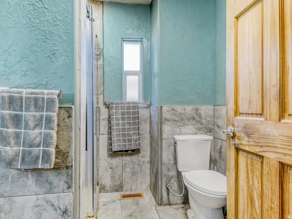 Full bathroom with a textured wall, a wainscoted wall, tile walls, and a shower stall