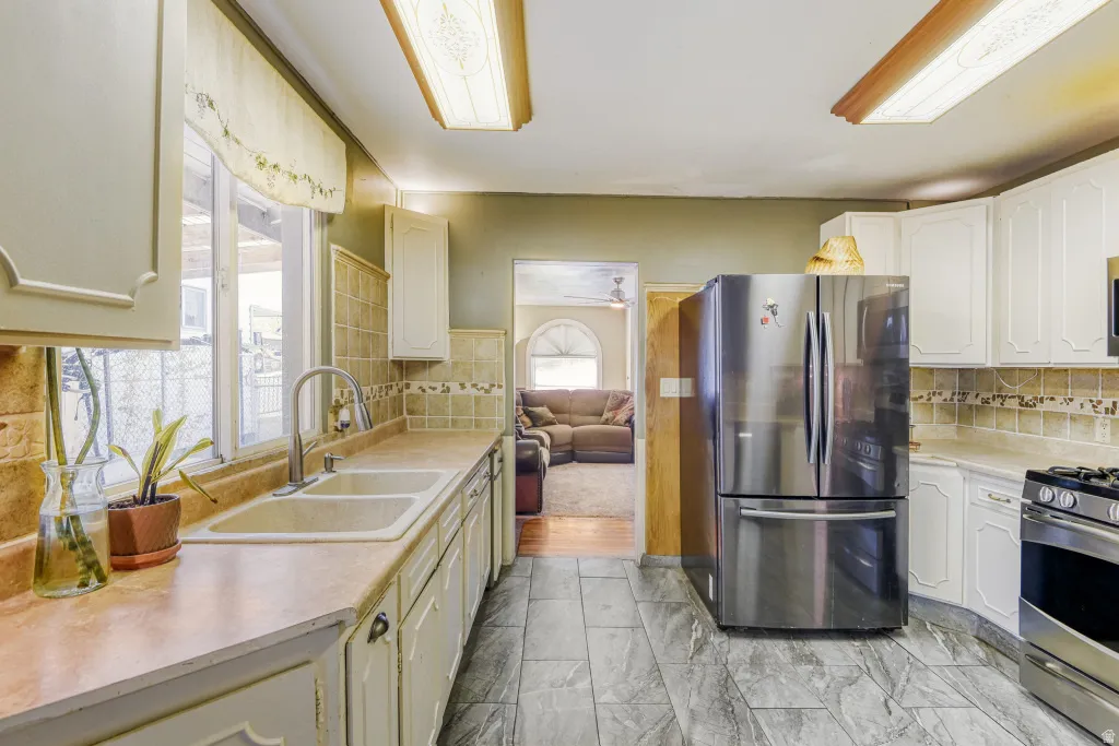 Kitchen featuring stainless steel appliances, light countertops, decorative backsplash, white cabinets, and light marble finish floors