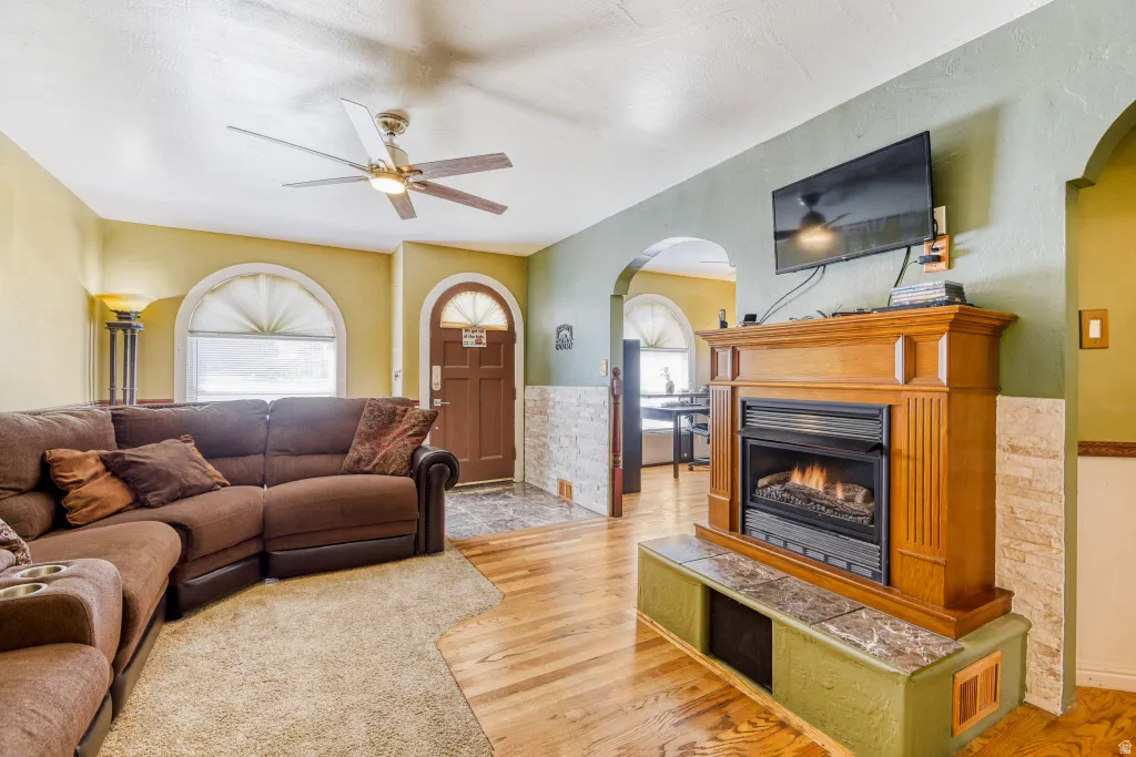 Living area with arched walkways, light wood-type flooring, ceiling fan, and a glass covered fireplace