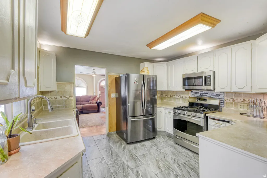 Kitchen with stainless steel appliances, white cabinetry, light countertops, and light marble finish floors
