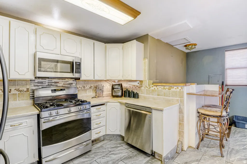 Kitchen with stainless steel appliances, light countertops, a breakfast bar area, a peninsula, and white cabinets