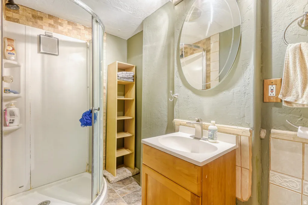 Full bathroom featuring vanity, a stall shower, a textured ceiling, and a textured wall
