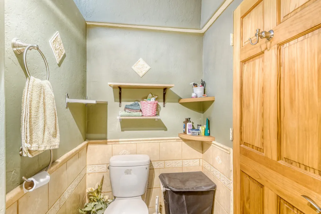 Half bathroom with a textured wall, a wainscoted wall, and tile walls