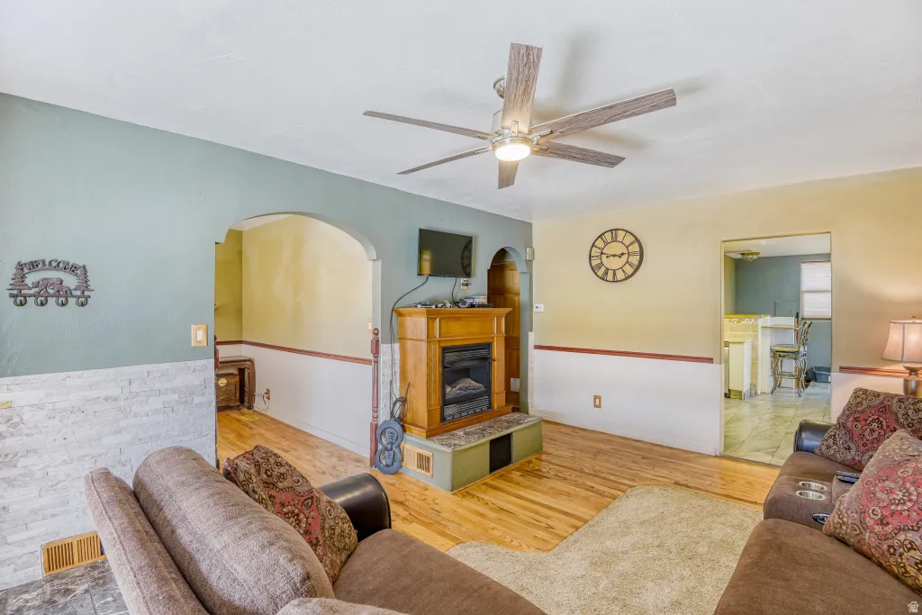 Living room with light wood-style floors, ceiling fan, and a glass covered fireplace