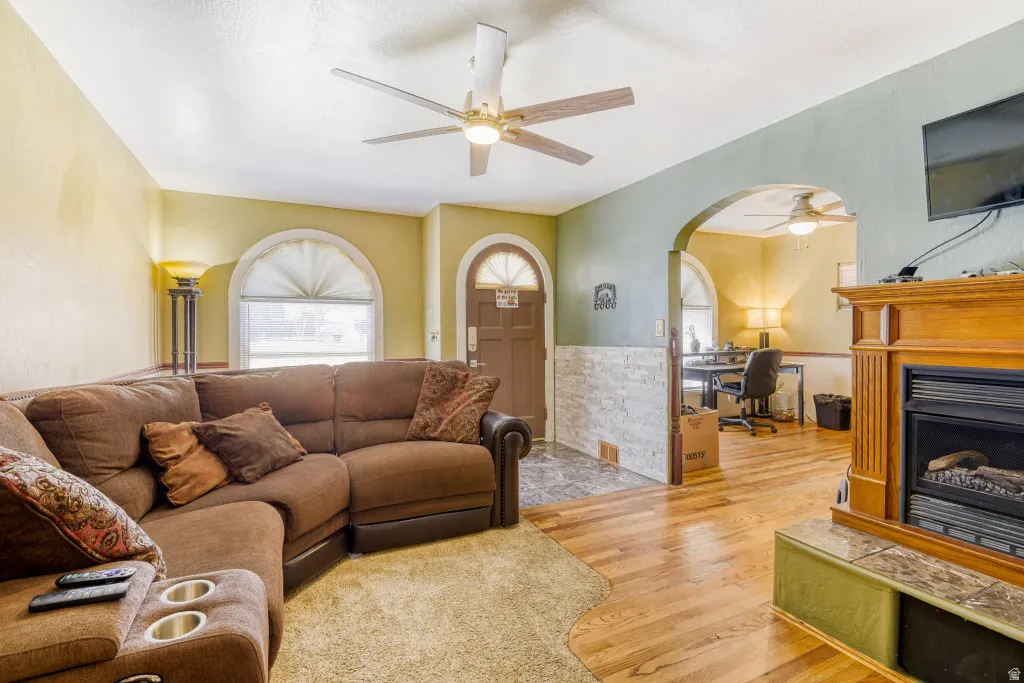 Living area featuring light wood-style floors, arched walkways, an office area, a ceiling fan, and a fireplace with raised hearth