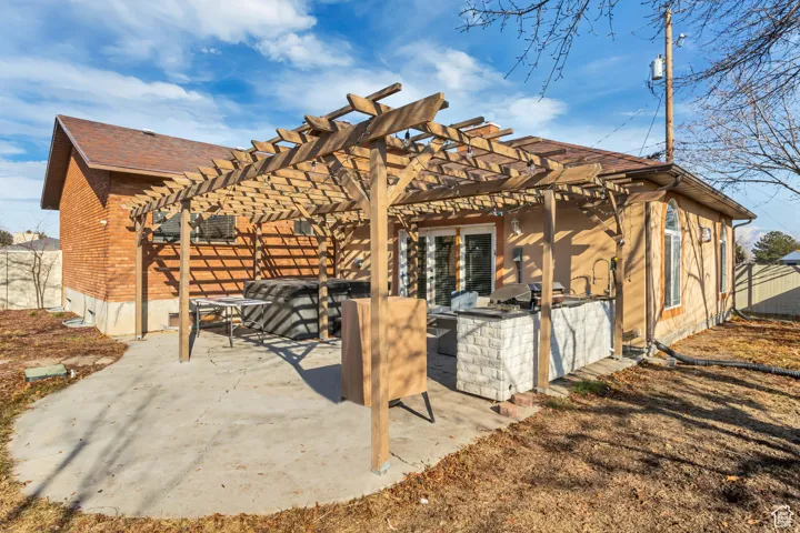 Exterior patio featuring a wood pergola, concrete patio surface, and a built-in outdoor kitchen with stone-finish cabinetry