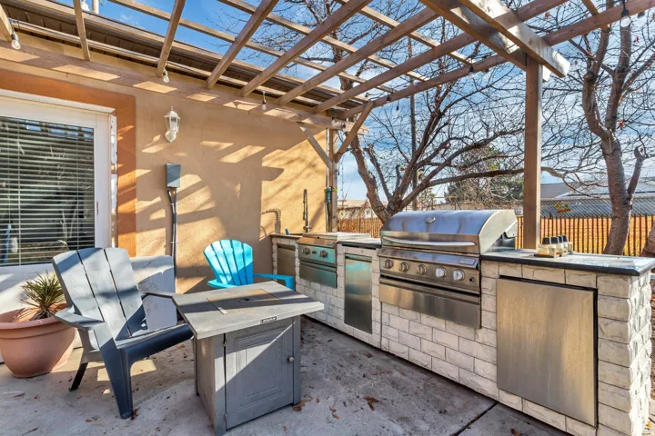 Patio featuring a wood pergola, stucco exterior, built-in outdoor kitchen with stainless steel appliances, and a light-colored brick base