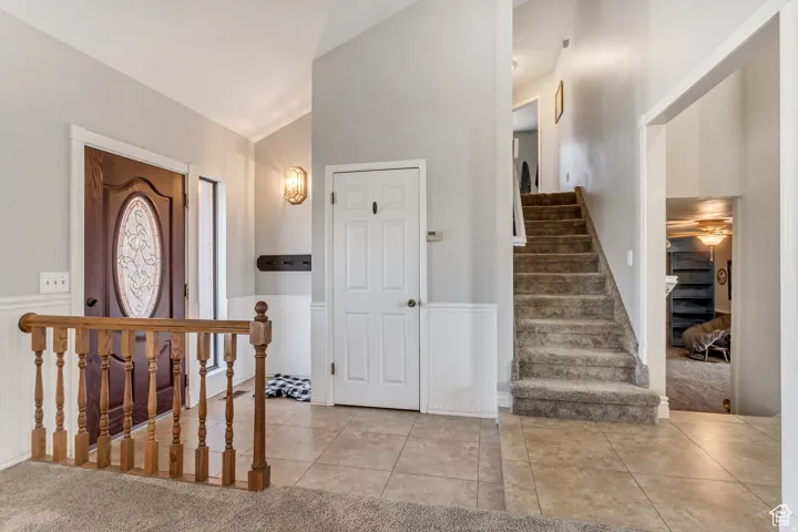 Entryway featuring a wood-panel front door with decorative glass, wainscoting, tile flooring, and a carpeted staircase