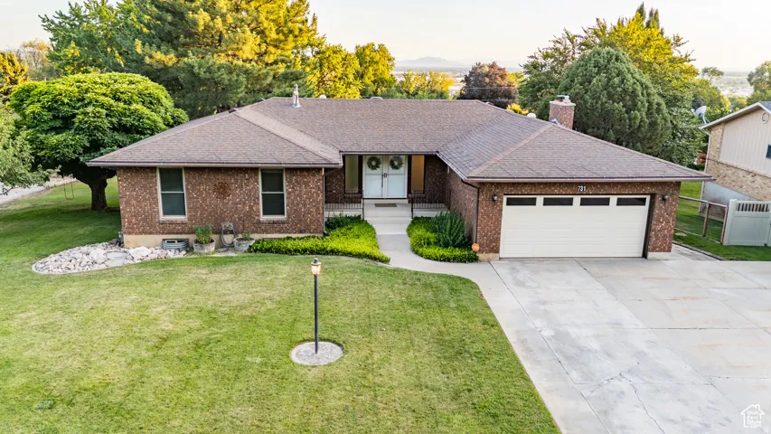Ranch-style home featuring a garage, driveway, brick siding, and roof with shingles