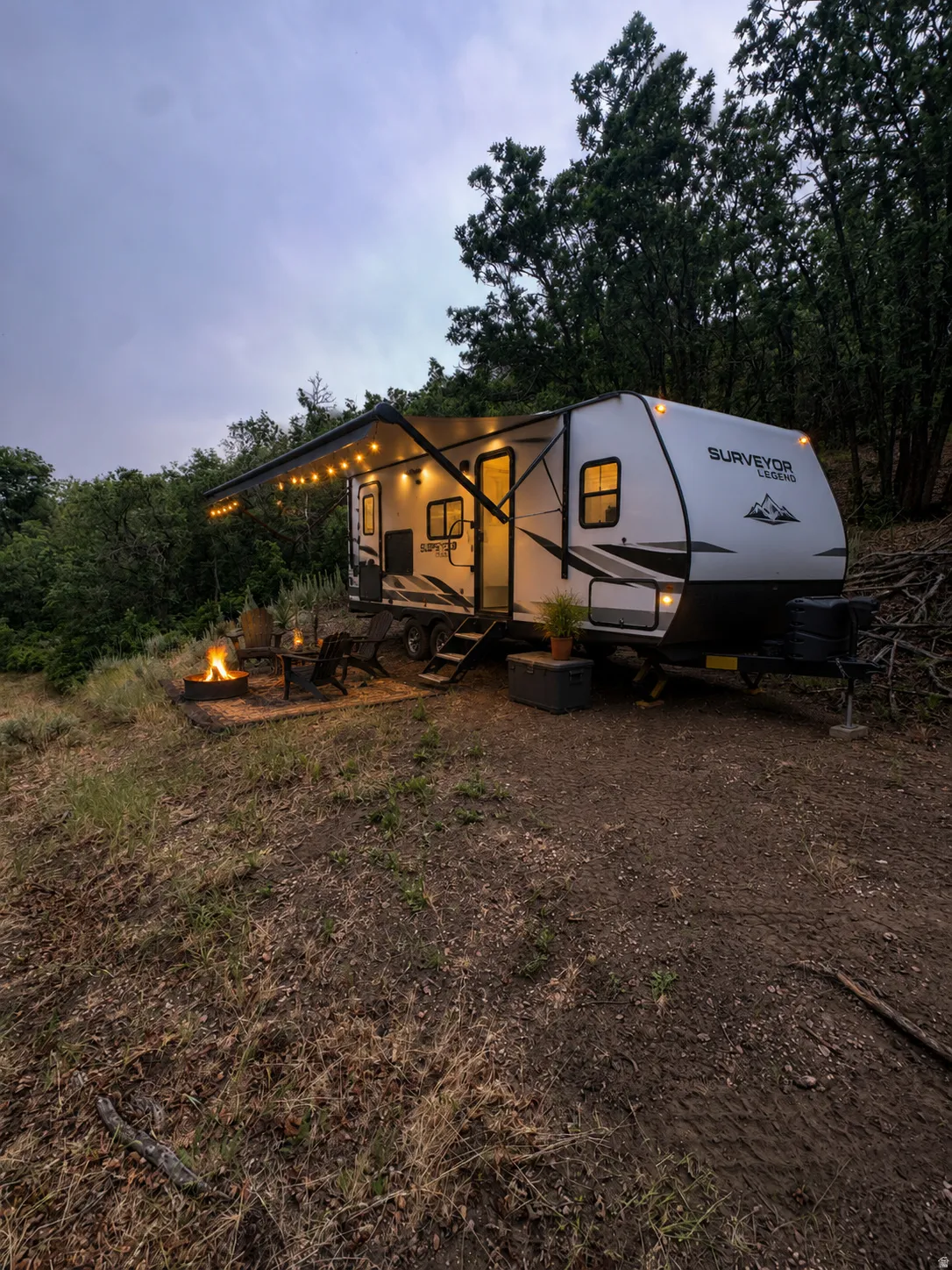 Modern travel trailer featuring a light-colored exterior, an extendable awning with string lights, and multiple windows