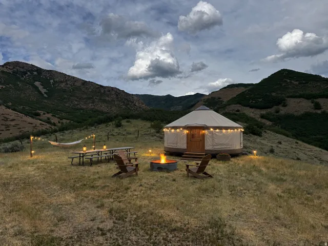 Freestanding yurt structure with a wood entry door on a sloped, vegetated landscape