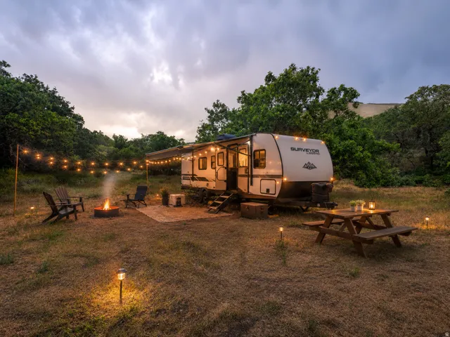Recreational vehicle campsite featuring a fire pit, string lighting, and ground lights