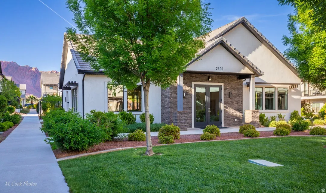View of front of property with french doors, stucco siding, a front lawn, and brick siding