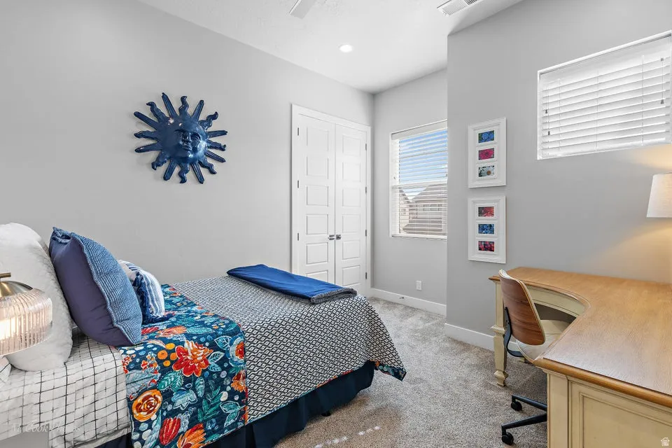 Bedroom with light colored carpet, a ceiling fan, and an office area