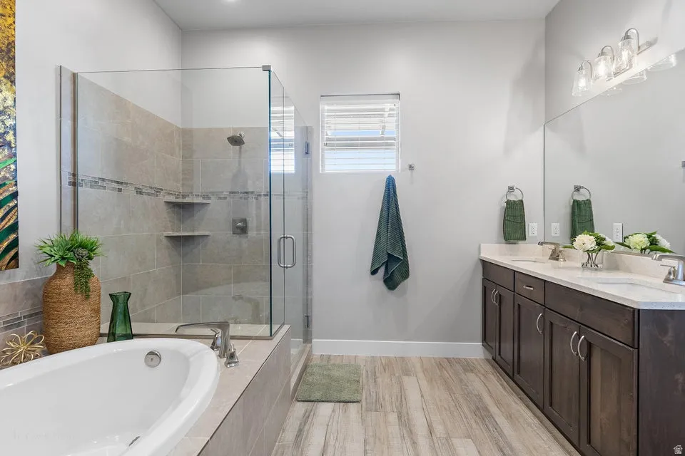 Bathroom featuring double vanity, a bath, a stall shower, and light wood-style flooring