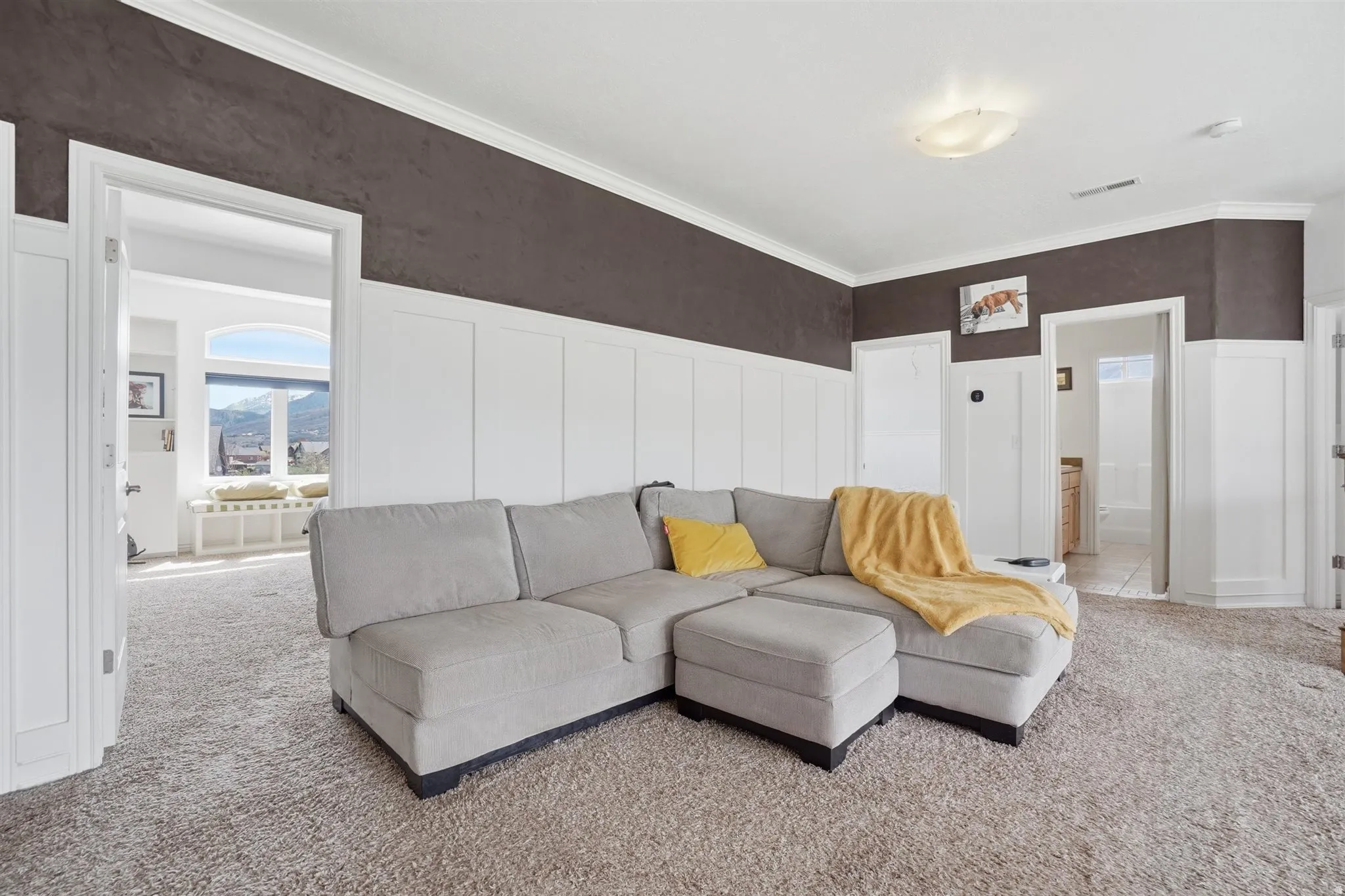Living room with a decorative wall, wainscoting, crown molding, and carpet floors