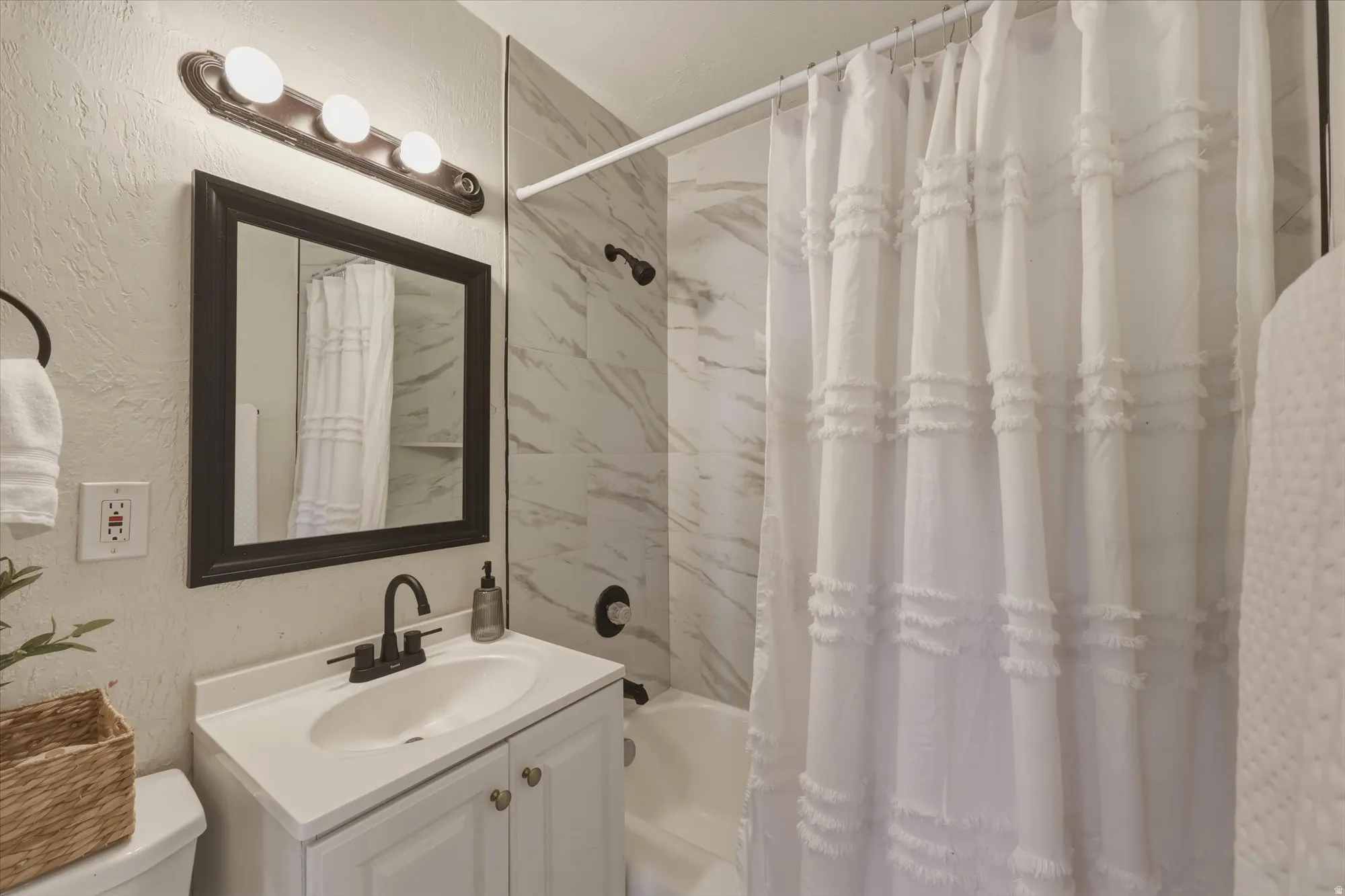 Full bath with vanity, a textured wall, and shower / bath combo