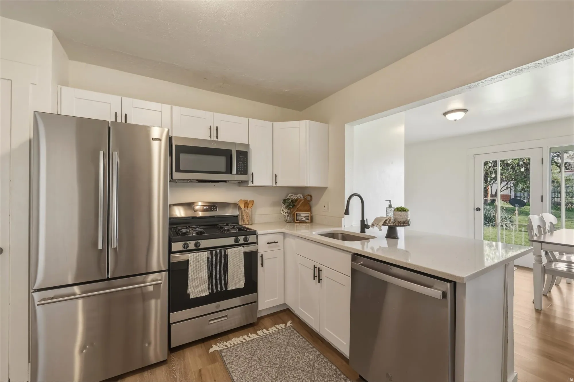 Kitchen featuring stainless steel appliances, light wood-style floors, white cabinets, and light stone countertops