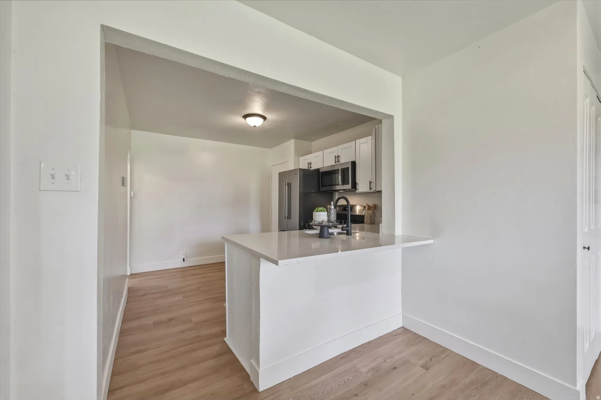 Kitchen with light wood-type flooring, white cabinetry, stainless steel microwave, a peninsula, and a kitchen bar