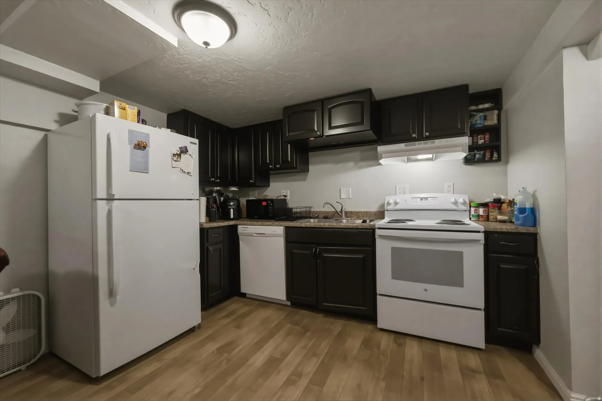 Kitchen with white appliances, light wood finished floors, a textured ceiling, and dark cabinetry