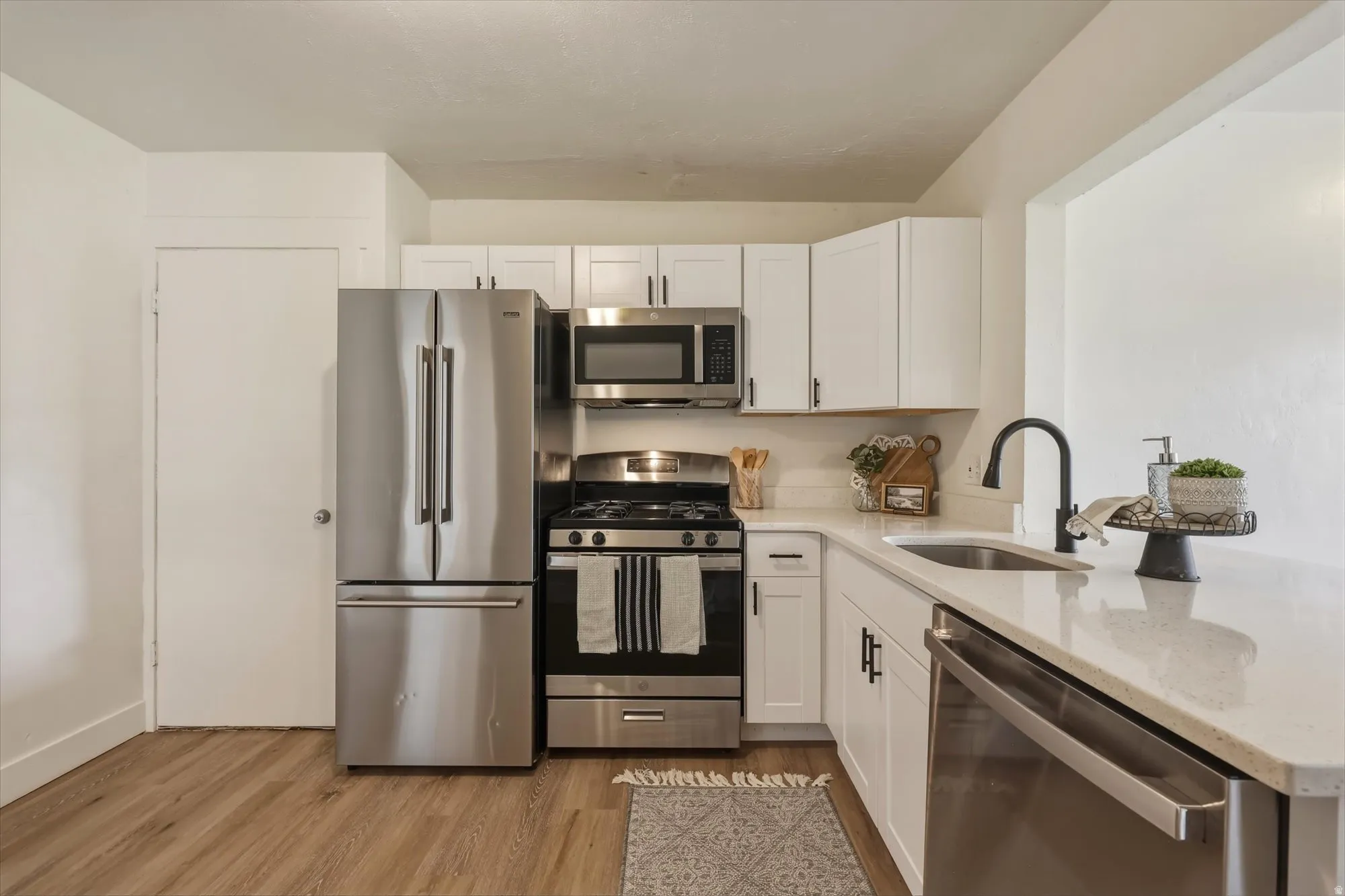Kitchen featuring stainless steel appliances, light stone countertops, white cabinetry, and light wood finished floors