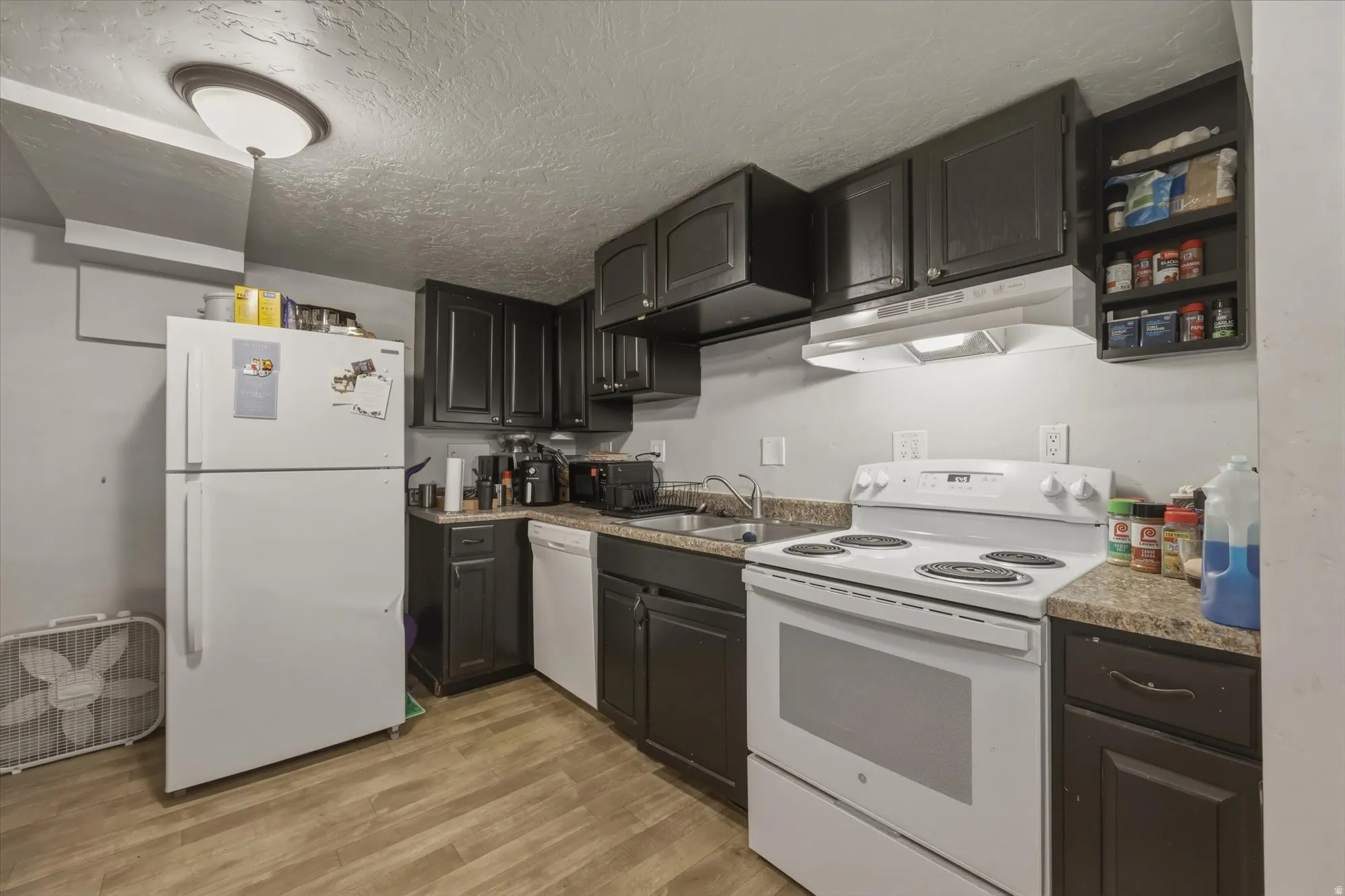 Kitchen featuring white appliances, light wood-style floors, and a textured ceiling