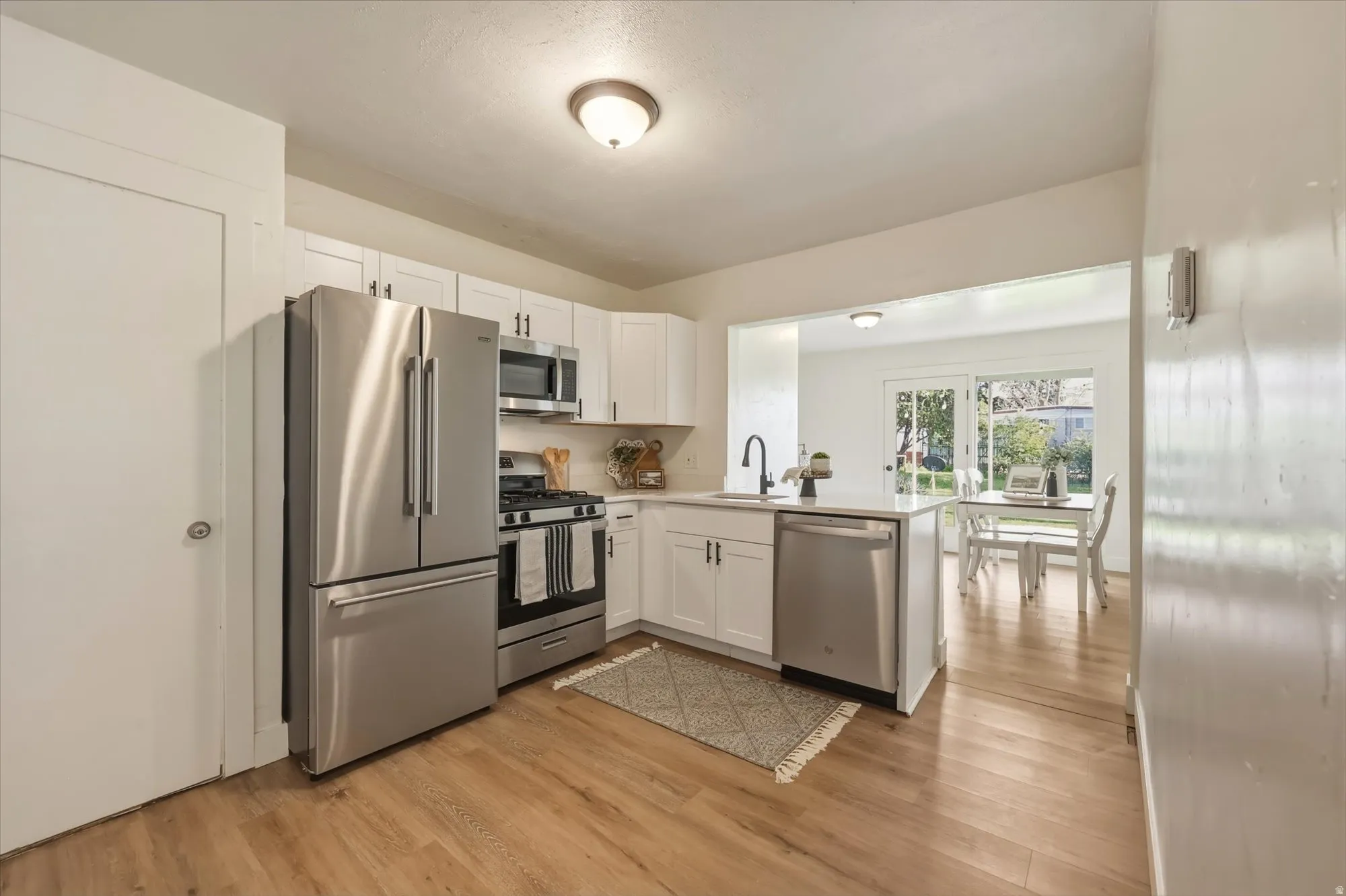 Kitchen with stainless steel appliances, white cabinetry, light wood-type flooring, and a peninsula
