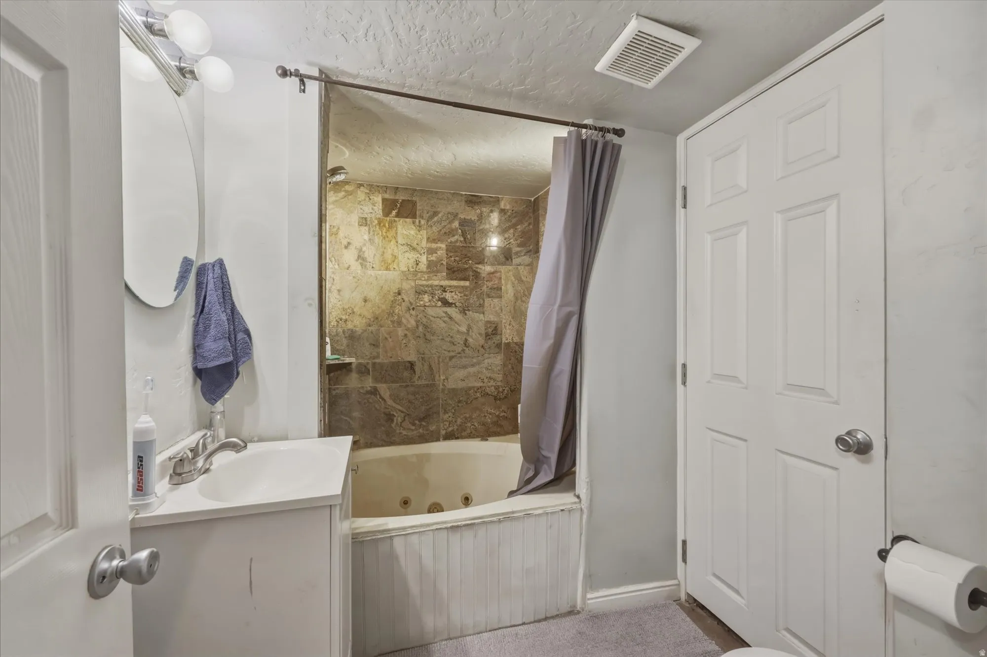Bathroom featuring a textured ceiling, vanity, and a combined bath / shower with jetted tub