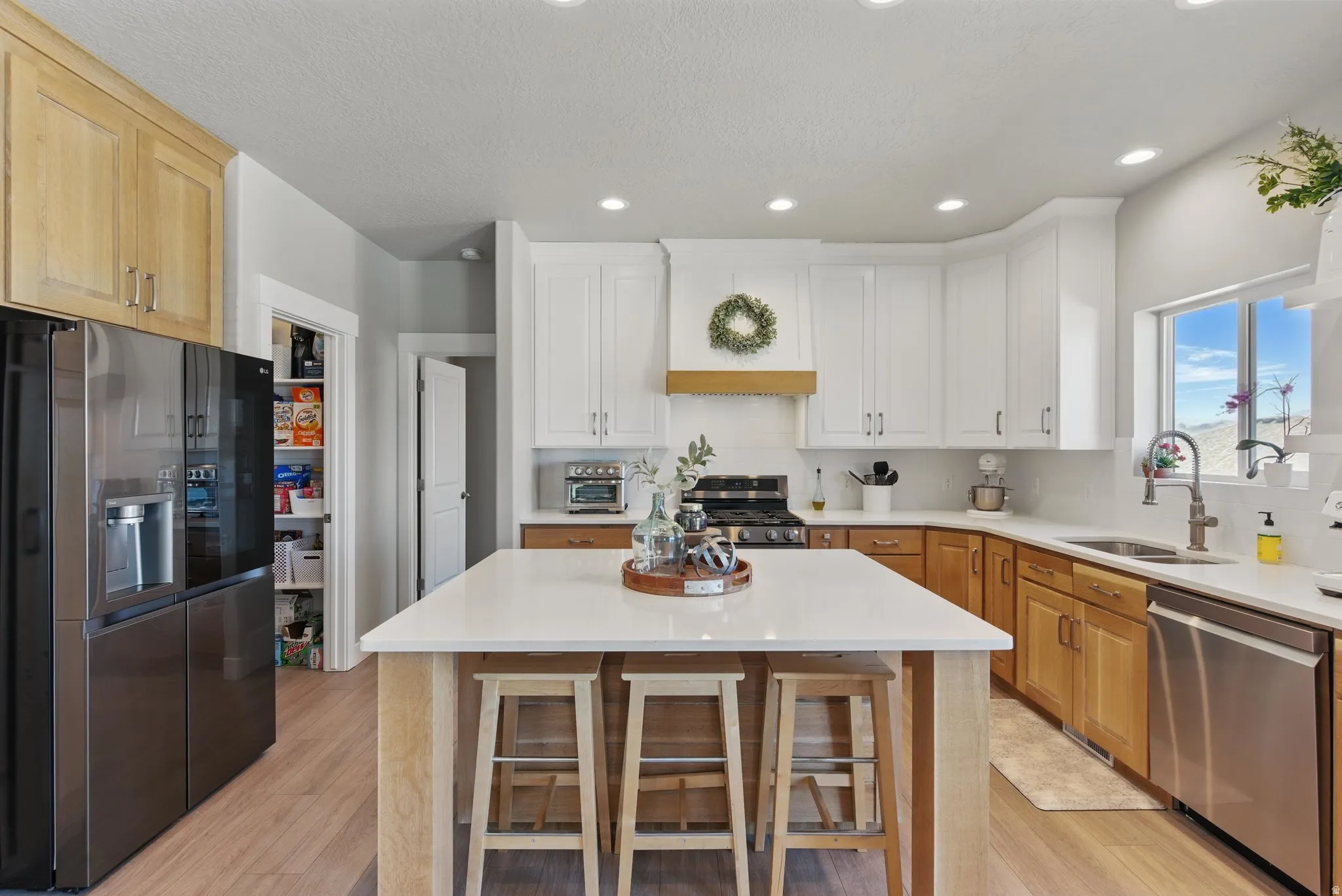 Two tone kitchen with stainless steel appliances, recessed lighting, a center island, light wood-type flooring, and two tone cabinetry