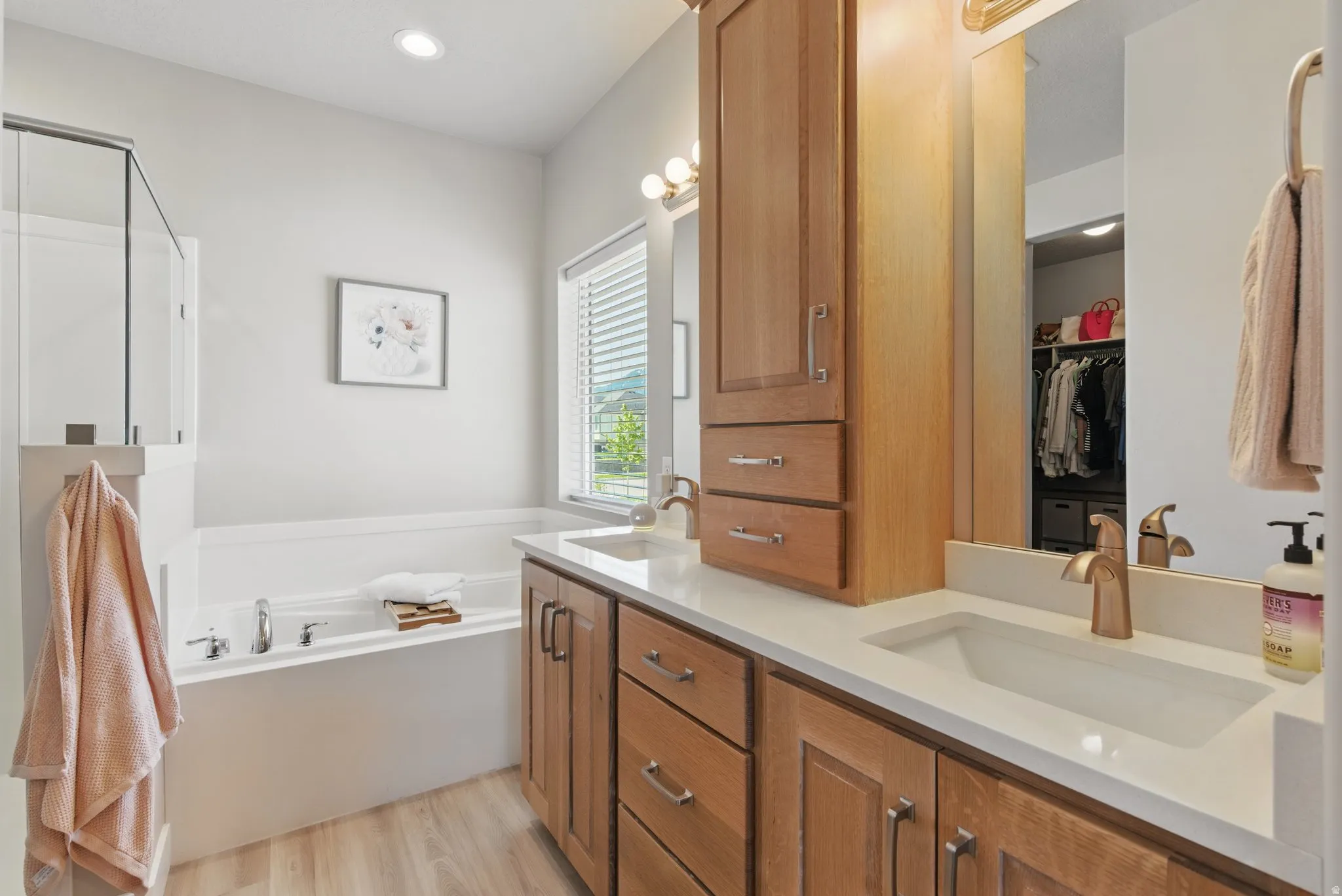 Bathroom featuring double vanity, a walk in closet, a garden tub, light wood-style floors, and recessed lighting